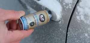 Mano aplicando un descongelador de cerraduras K2 en la cerradura de una puerta de automóvil, que está cubierta de nieve y hielo