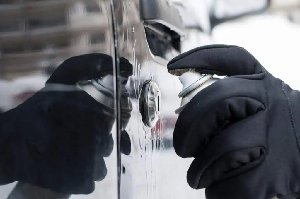 Mano con guantes negros aplicando un spray descongelador en la cerradura de la puerta de un automóvil en invierno